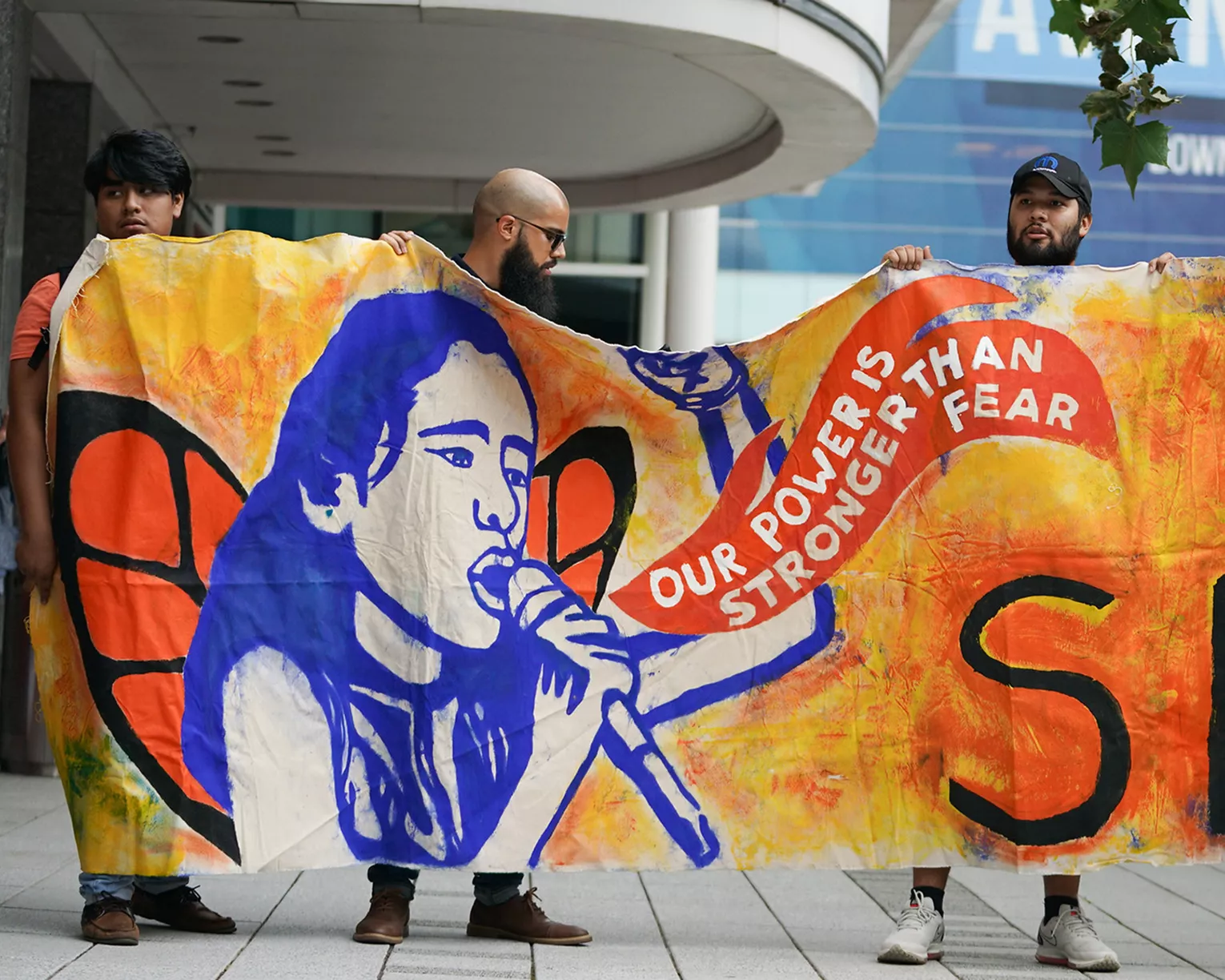 3 activists hold a banner protesting immigration policy