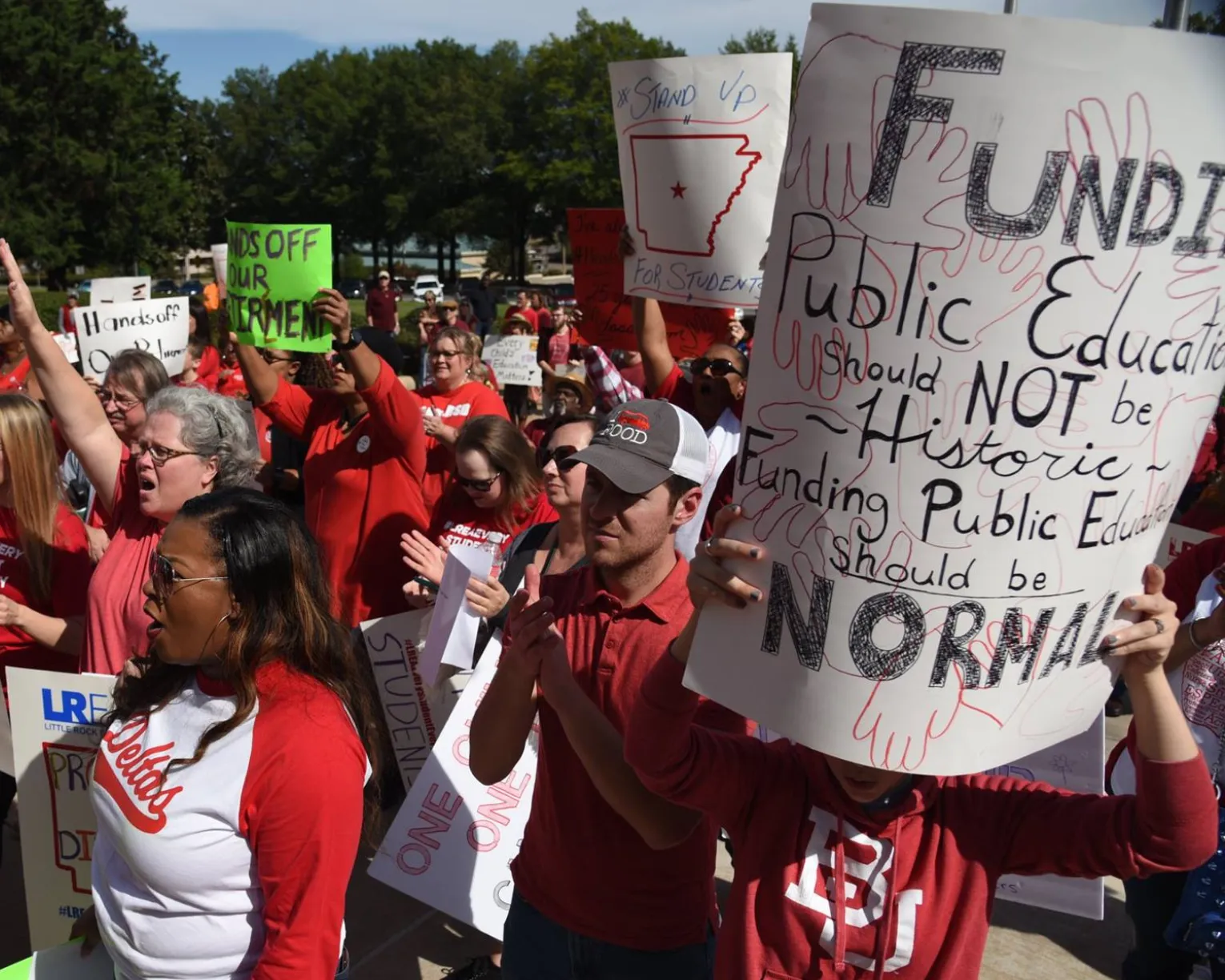 AEA members gathered in a crowd at a statehouse rally. One member holds a sign that says, "Funding public education should not be historic. Funding public education should be normal."