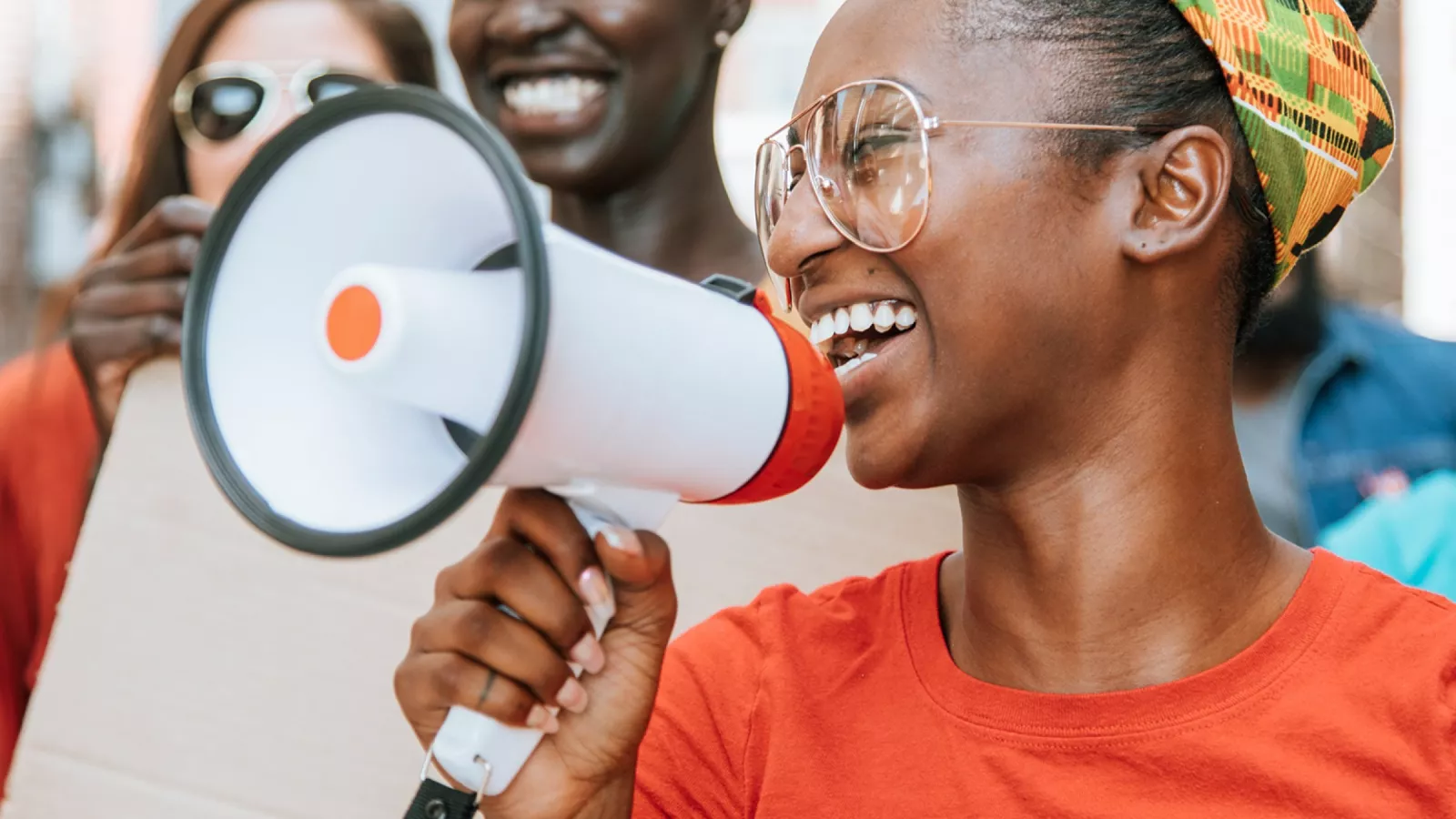 A young black woman smiles as she holds a megaphone and speaks to a picket line