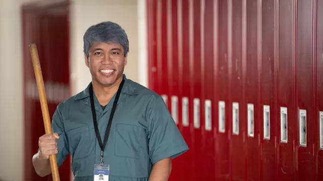 A custodian stands in a hall smiling