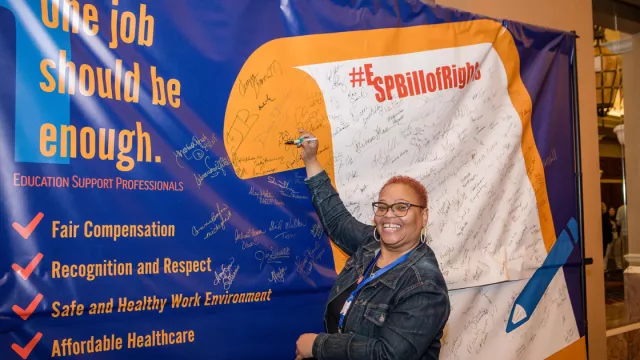 An NEA member signing a large banner of the ESP Bill of Rights